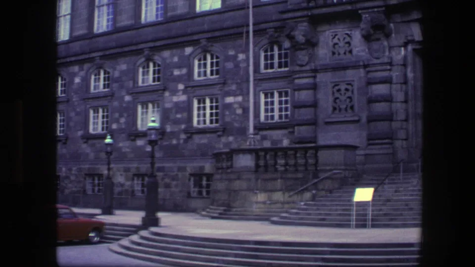 1975 Copenhagen exterior showing the building's stone wall, arched windows, broad steps, lampposts, and a small signboard near the entrance.