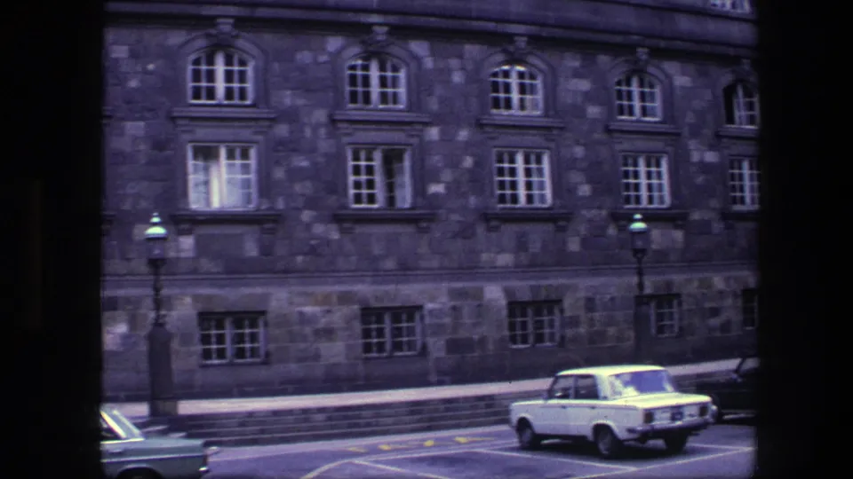1970s Copenhagen street view with a stone institutional-looking facade, arched windows, streetlamps and classic cars near the curb.