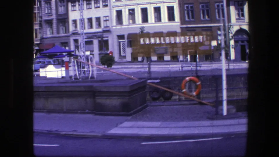 Copenhagen waterfront street frame from 1975 showing canal railings, a life ring, storefront lettering, and multi-story building facades.