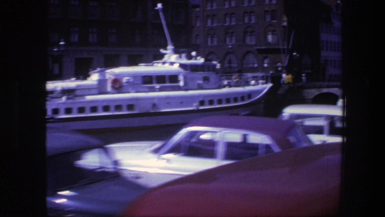 White ferry beside waterfront buildings with blurred cars in the foreground.