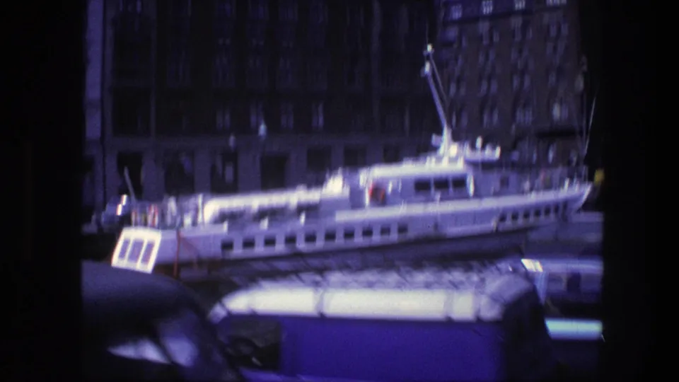 Handheld 8mm view of a docked white ferry along a Copenhagen waterfront, with buildings behind and a vehicle roof crossing the lower frame.