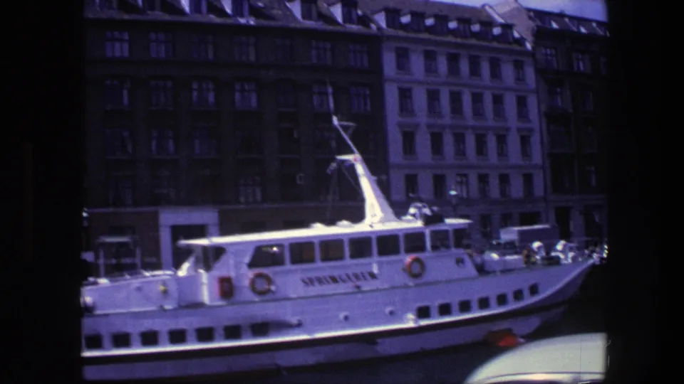 The SPRINGEREN passenger boat sits along a Copenhagen waterfront in 1975, with parked classic cars and tall buildings visible behind it.