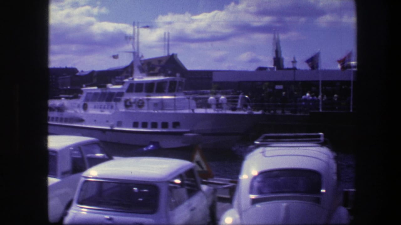Parked cars in front of a white passenger boat at a Copenhagen harbor.