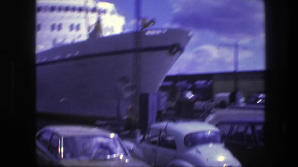 1975 Copenhagen harbor frame showing the bow of a large white ship rising above parked cars along the waterfront.