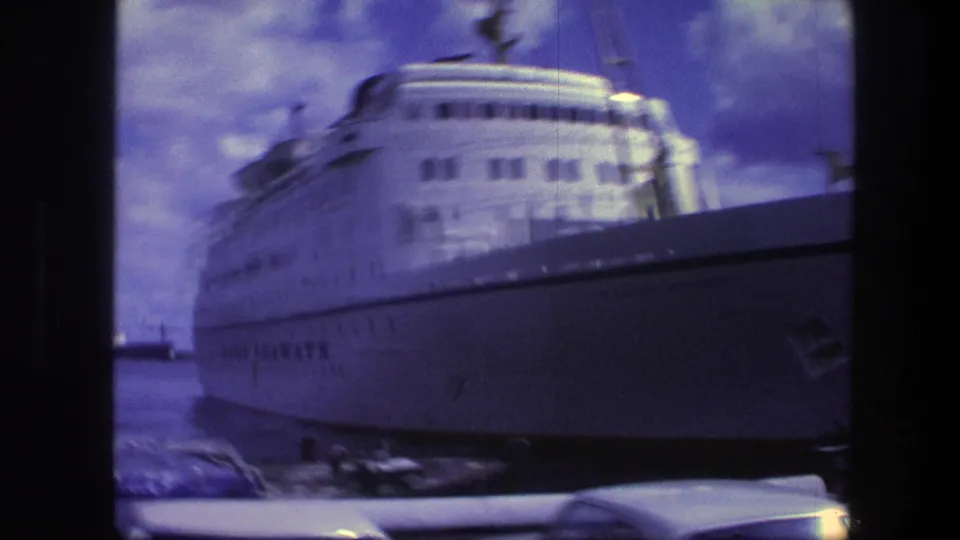 1975 Copenhagen harbor view of a large white passenger ship, with classic cars low in the foreground and cloudy sky above.
