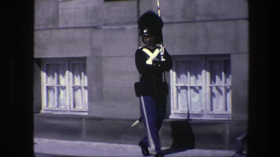 A uniformed ceremonial soldier marches outside a stone building in Copenhagen, Denmark, in 1975 home-movie footage.