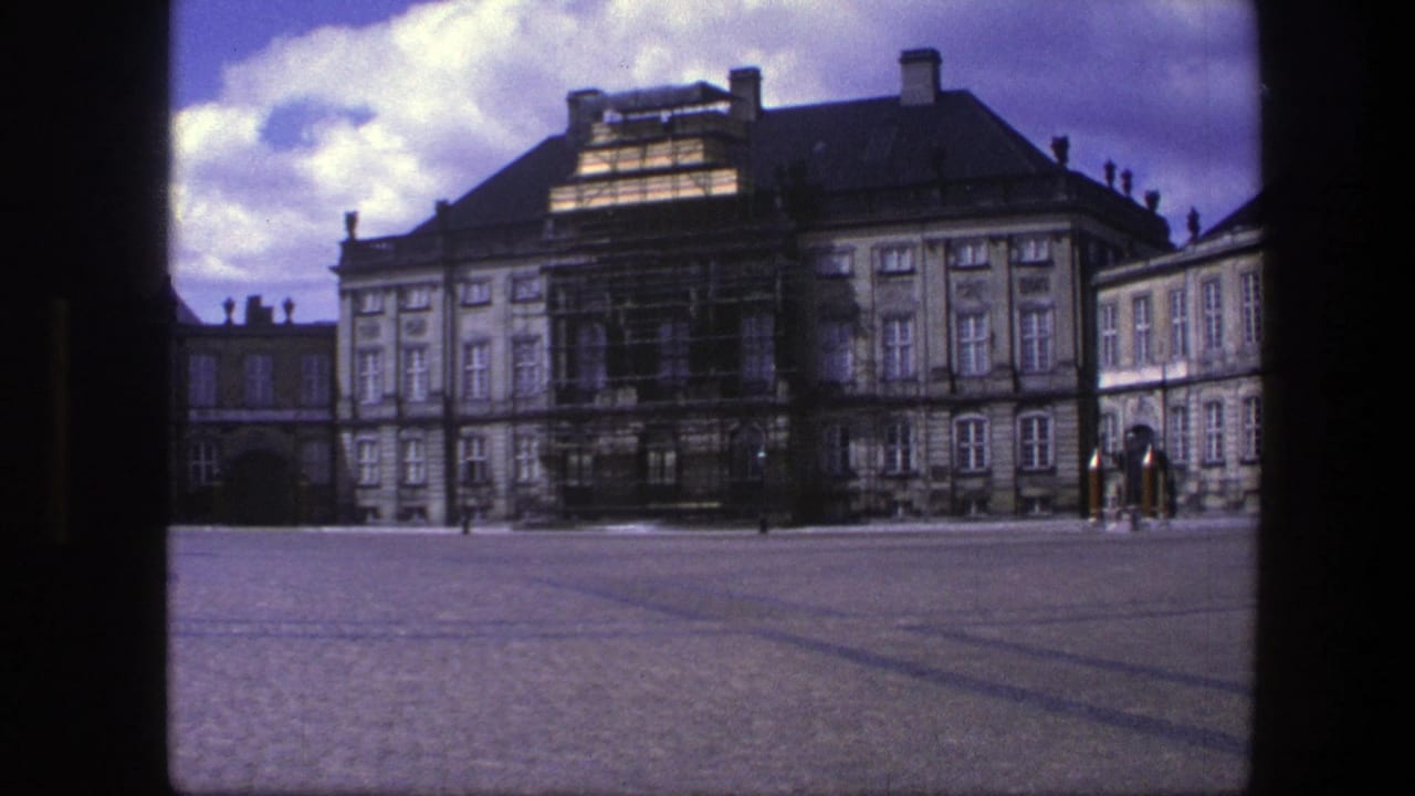 Wide courtyard view of the palace facade with scaffolding and distant figures by a guard post.