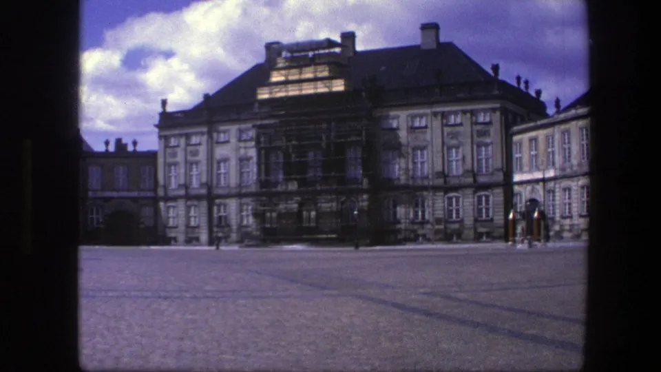 1975 Copenhagen frame of a palace courtyard with restoration scaffolding, tall windows, cloudy sky, and distant visitors or guards.