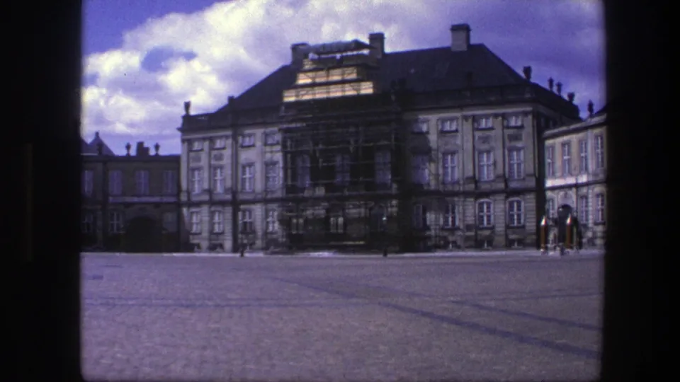 1975 Copenhagen home-movie view of a palace exterior, showing scaffolding, an arched gateway, cobblestones, and distant people.