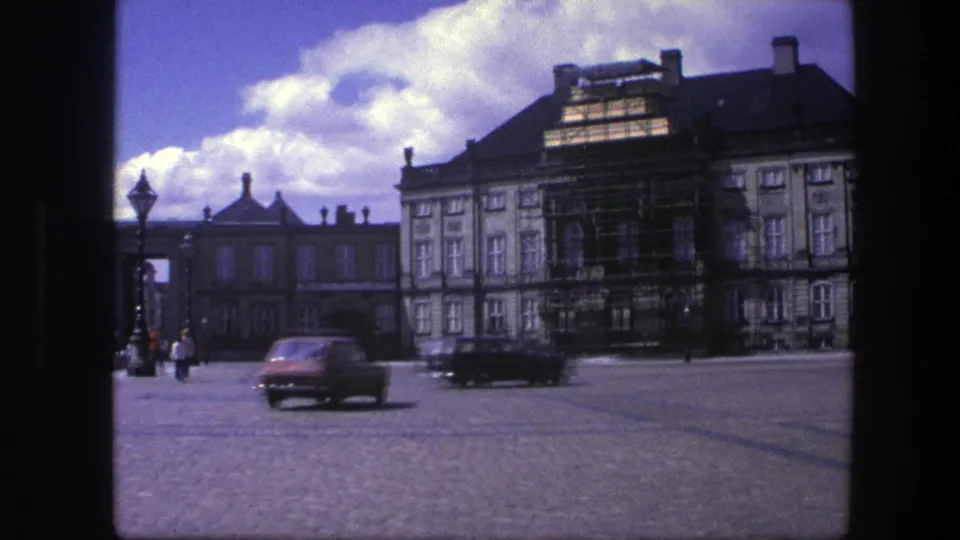 1975 Copenhagen traffic passes across Amalienborg courtyard in front of the scaffolded palace facade.