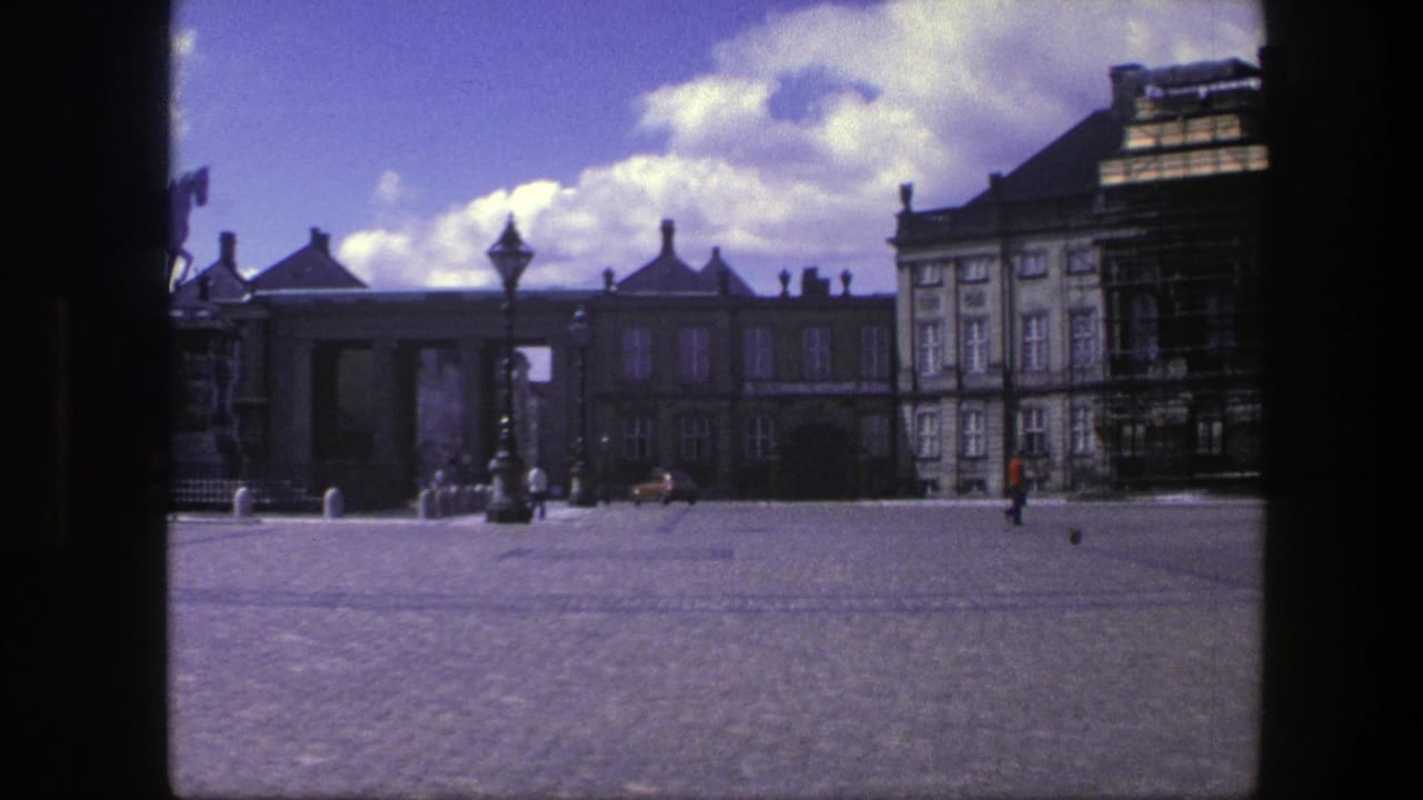 Wide cobblestone square with palace buildings, lamppost, pedestrians, and part of an equestrian statue.