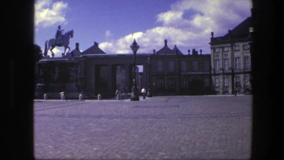 1975 Copenhagen frame showing the equestrian statue, palace facade, lamppost, open cobblestones, and a few distant pedestrians.
