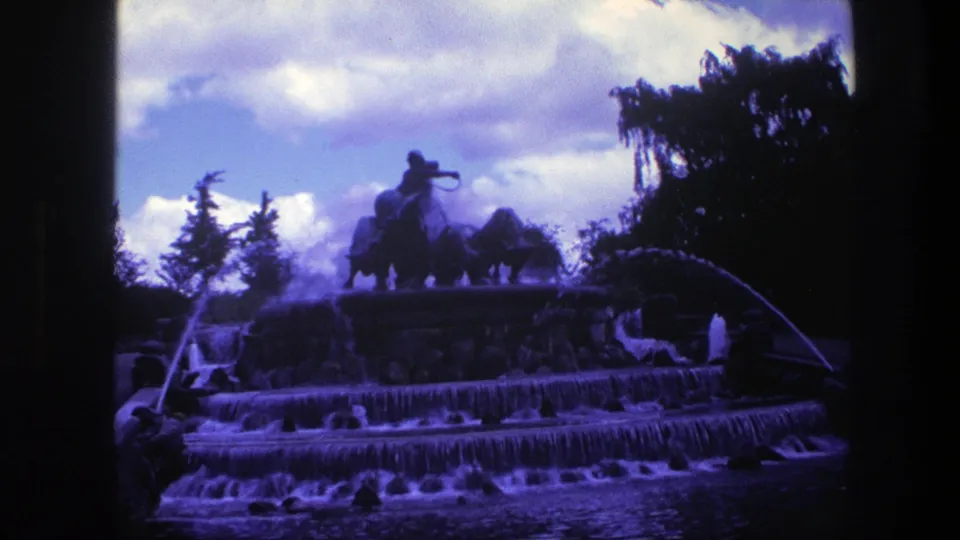 The 1975 Copenhagen footage holds on a wide fountain view with falling water, arcing jets, dark trees, and statue silhouettes at the top.