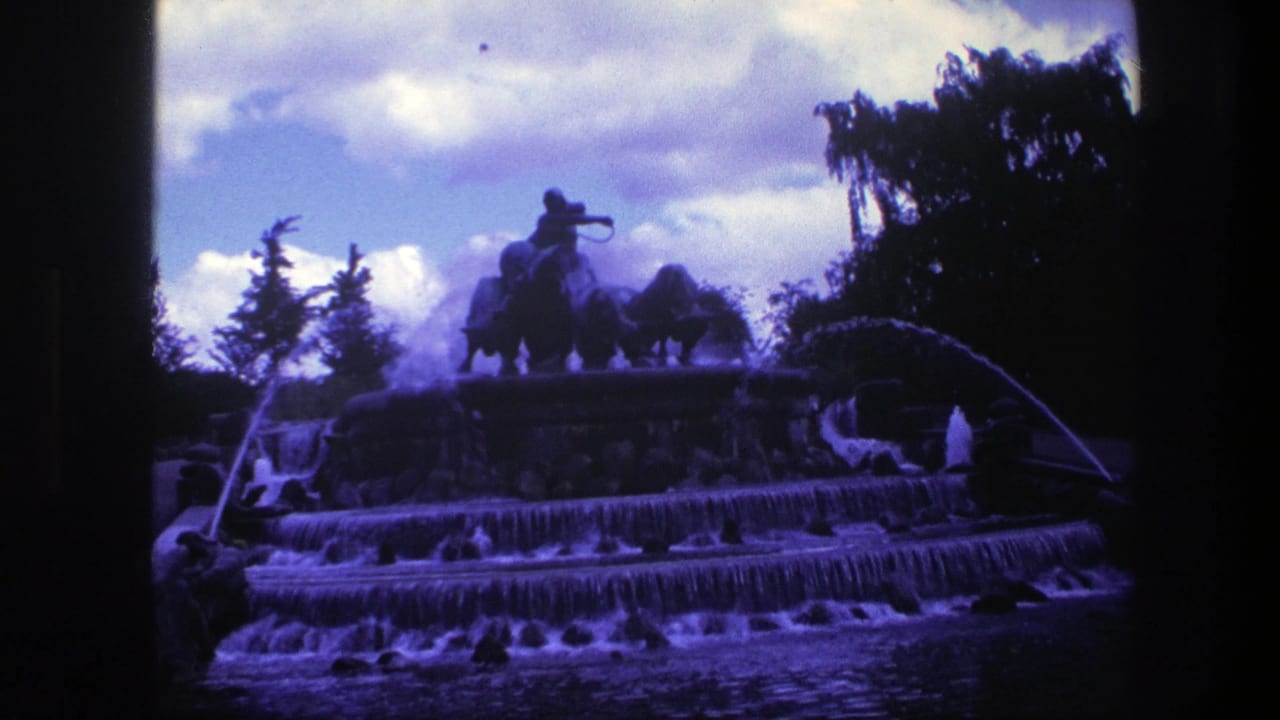 Multi-tier fountain with arcing water and a dark equestrian statue under cloudy sky.
