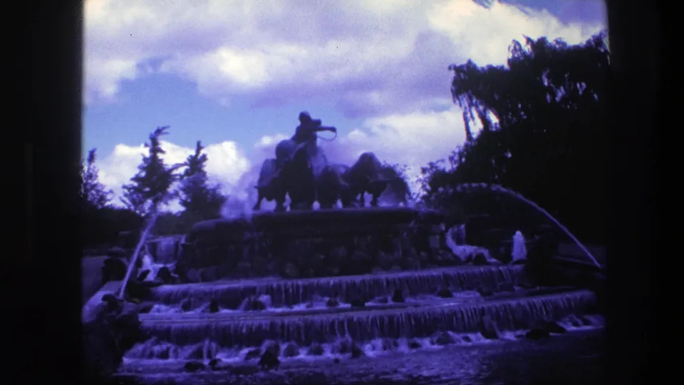 Vintage 8mm frame from Copenhagen showing a public fountain, falling water, arched side jets, and a silhouetted equestrian sculpture.