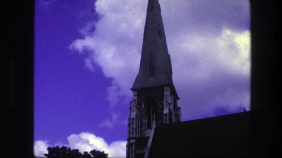 1975 Copenhagen 8mm frame with the church spire shifted right, a dark sloping roofline, clouded sky, and visible film-frame edge.