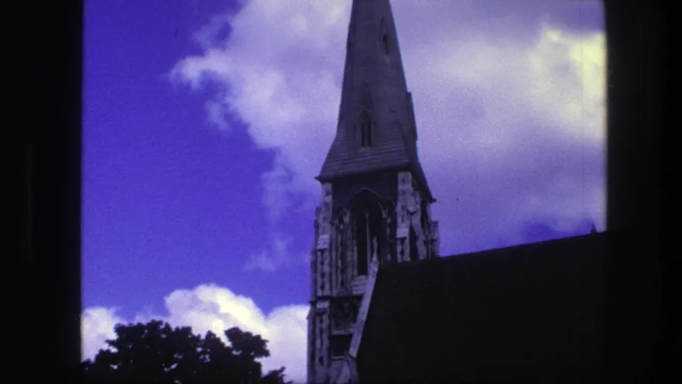 1975 Copenhagen 8mm frame showing the church tower and steep roof with treetops below and large white clouds behind the spire.