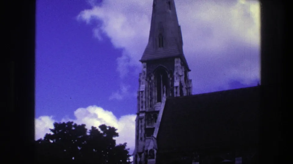1975 Copenhagen 8mm frame with a Gothic-style church steeple, dark roof mass, treetop silhouettes, and saturated blue-purple sky.