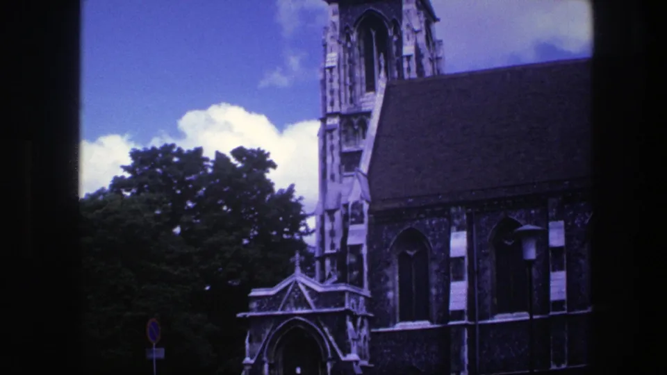 1975 Copenhagen home-movie frame showing the church entrance, front steps, stone facade, trees, and a small roadside sign.