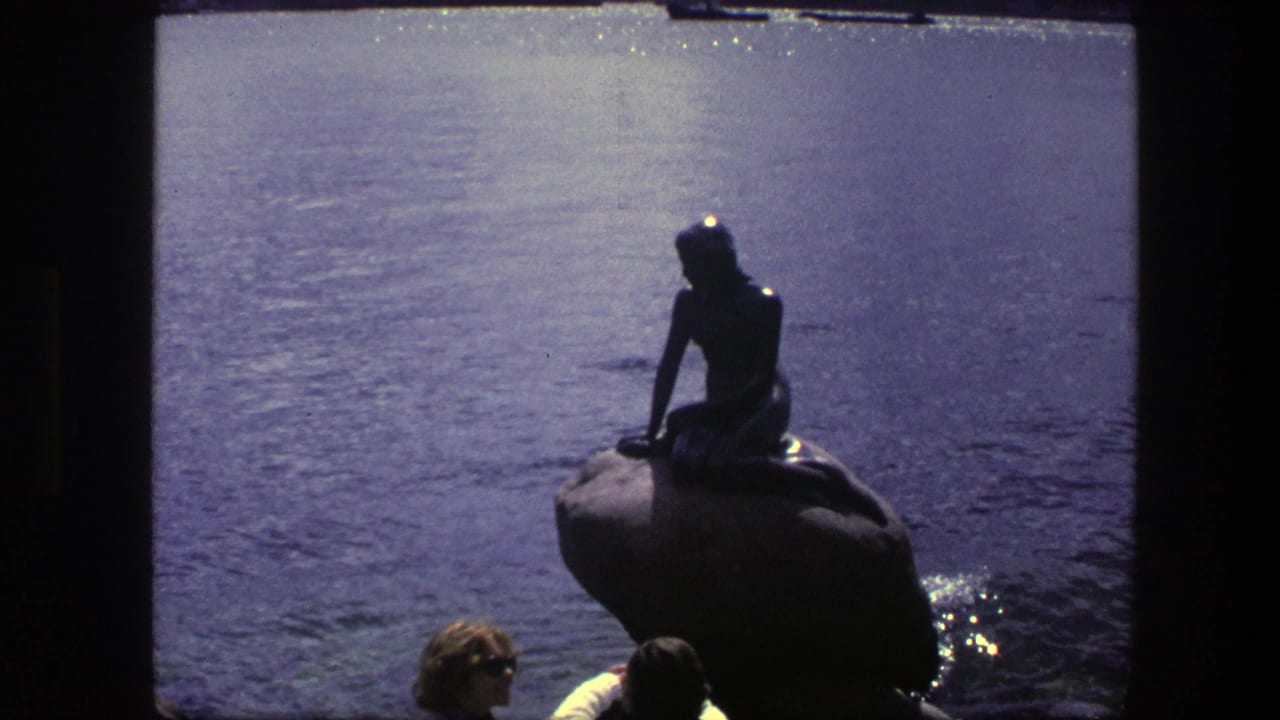 Little Mermaid statue silhouetted against water with visitors partly visible below.