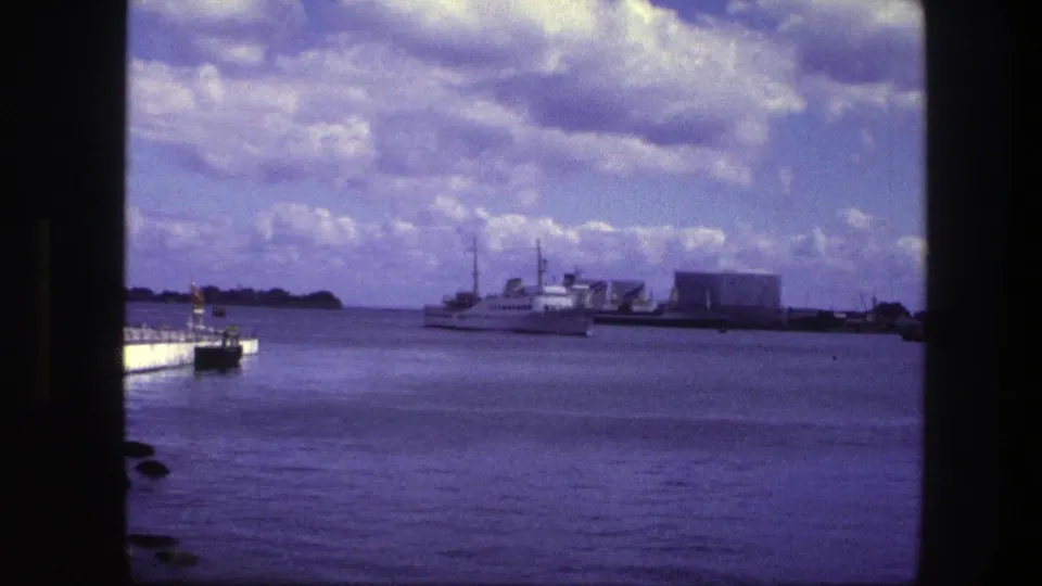 End frame of the 1975 Copenhagen harbor clip, with a white motorboat on purple-blue water and distant waterfront buildings under scattered clouds.