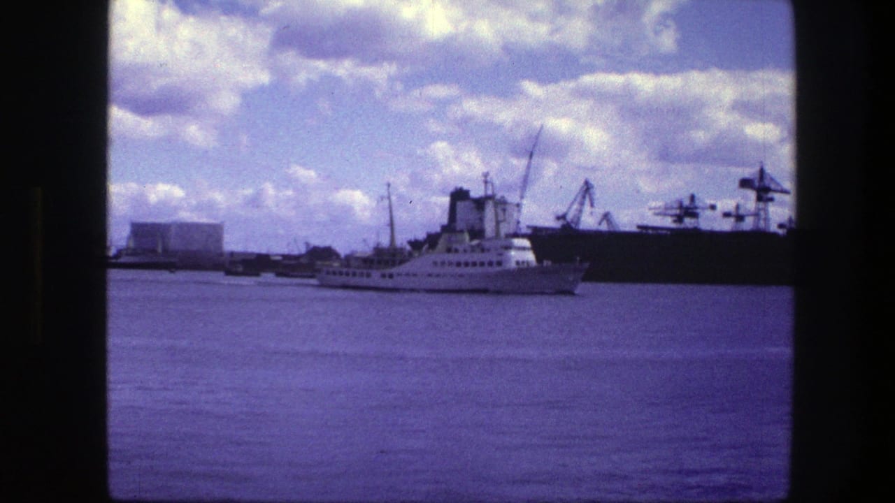 White ship farther across the harbor, backed by cranes, buildings, and cloud cover.