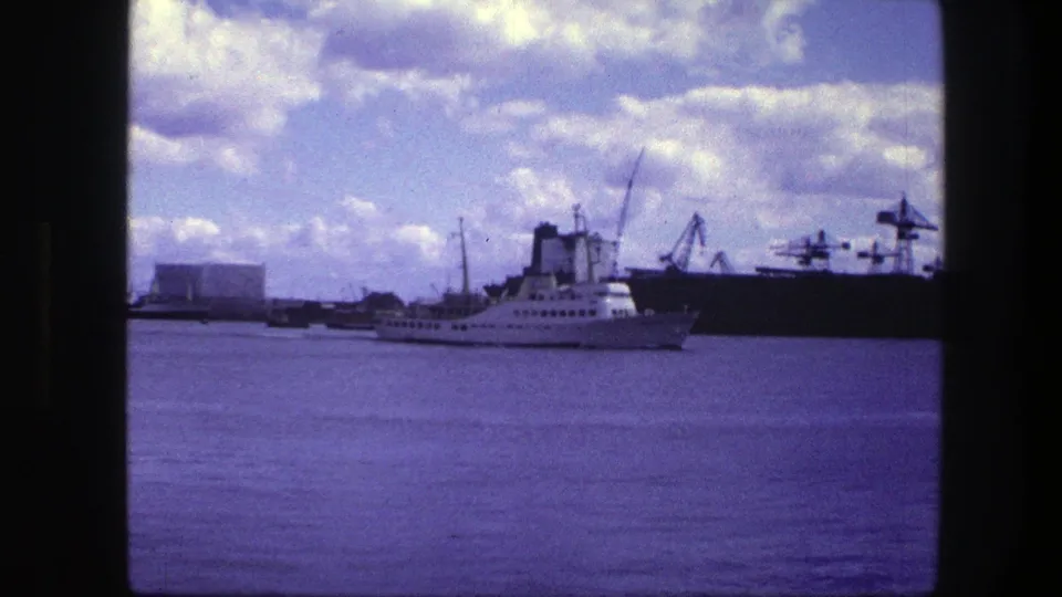 The 1975 Copenhagen harbor view holds on a white passenger ship passing industrial cranes along the waterfront.