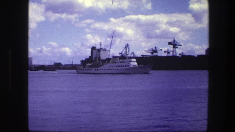 Near the end of the 1975 Copenhagen harbor clip, the white passenger ship passes cranes under a partly cloudy sky.