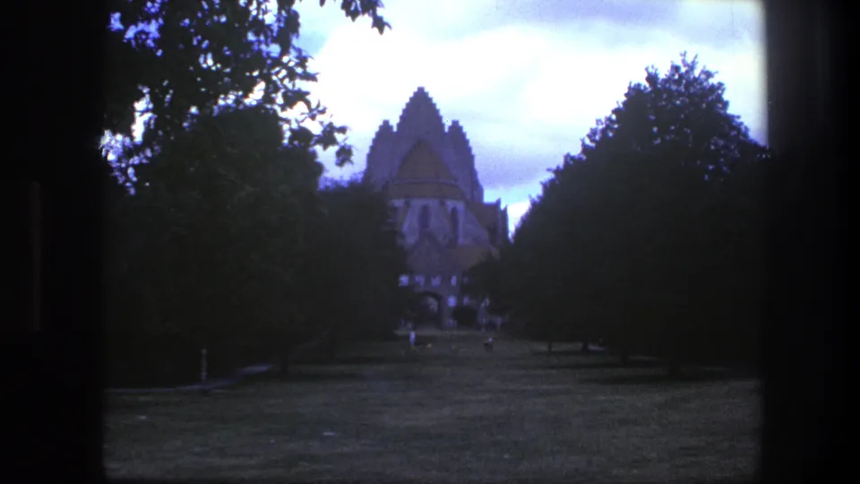 Copenhagen park view with a pointed church spire partly framed by trees and small distant visitors on the lawn.