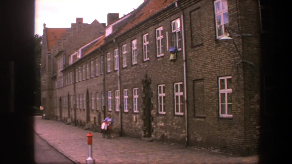 1975 Copenhagen street view with a lone person and bicycle beside a long brick building with white-framed windows.