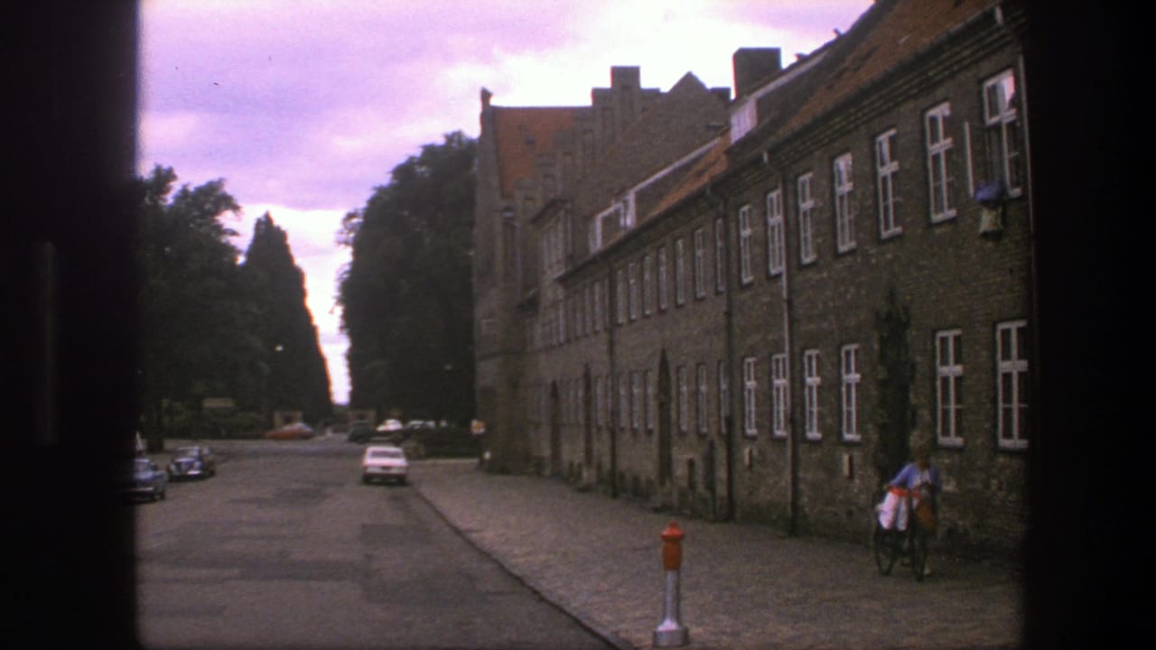 Street view framed by dark foreground with brick buildings, cars, and a cyclist.