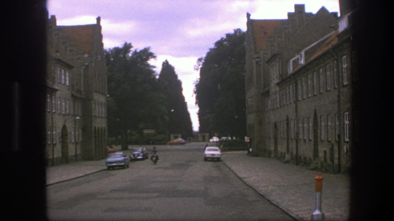 Distant moped rider and cars on a street lined with tall brick buildings.