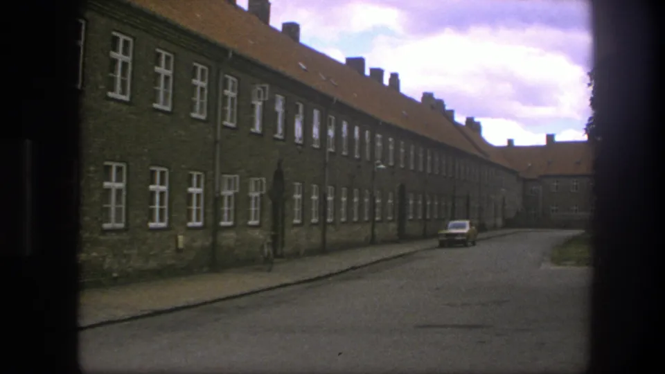 1975 Copenhagen street view showing brick buildings, repeated white windows, a parked car, and muted cloudy light.