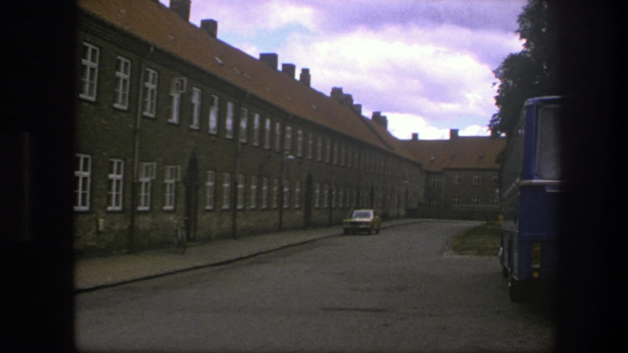 Brick street scene with parked car and the edge of a blue bus entering at right.