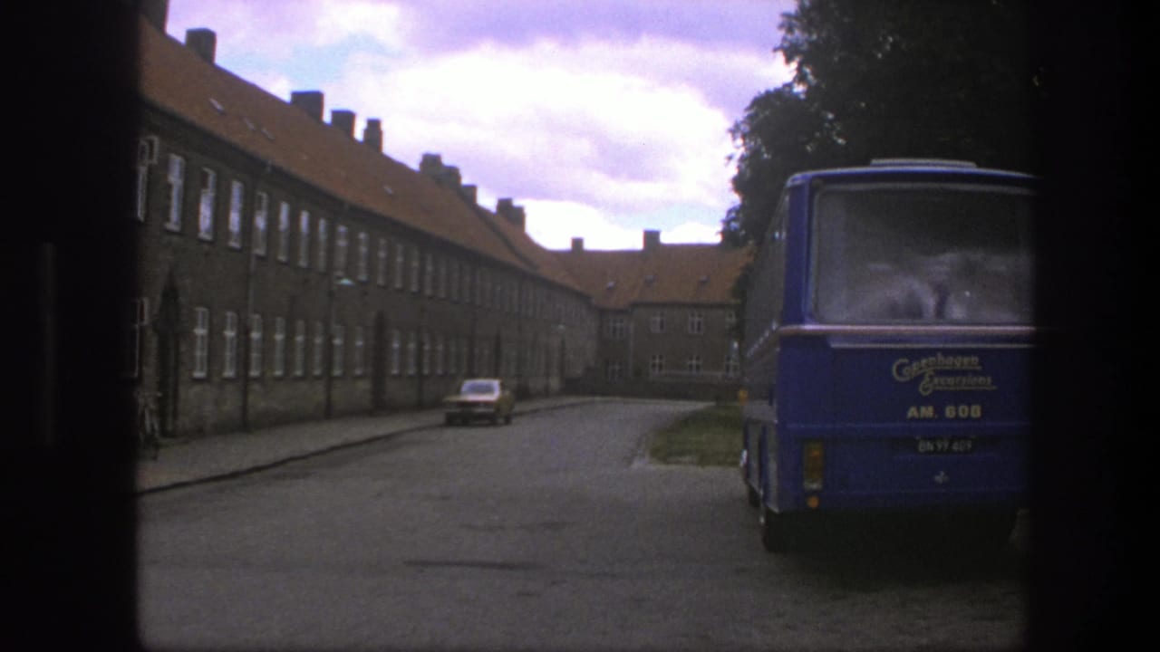 Blue bus parked on a cobblestone street beside long brick buildings under a cloudy sky.
