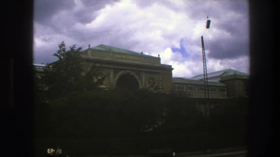 1975 Copenhagen view with a classical arched building, green roof, trees, cloudy sky, and dark vertical framing from the shooting position.