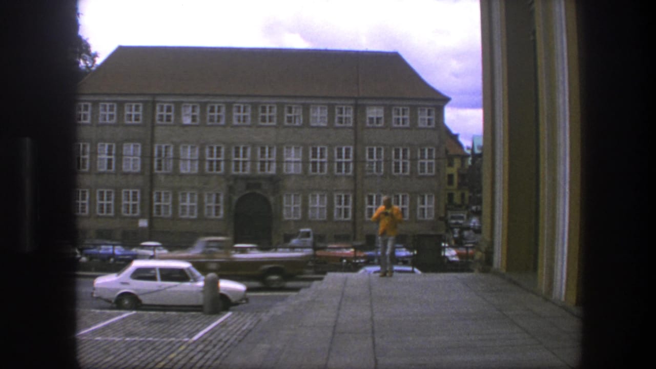 Doorway view of a Copenhagen street with parked cars and a man in a yellow jacket on the sidewalk.