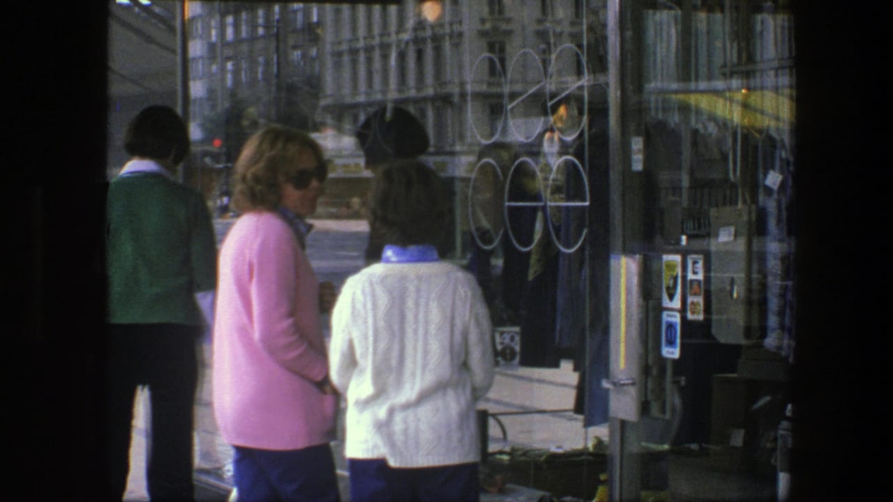 Two women stand at a glass storefront while another pedestrian is seen near the entrance.