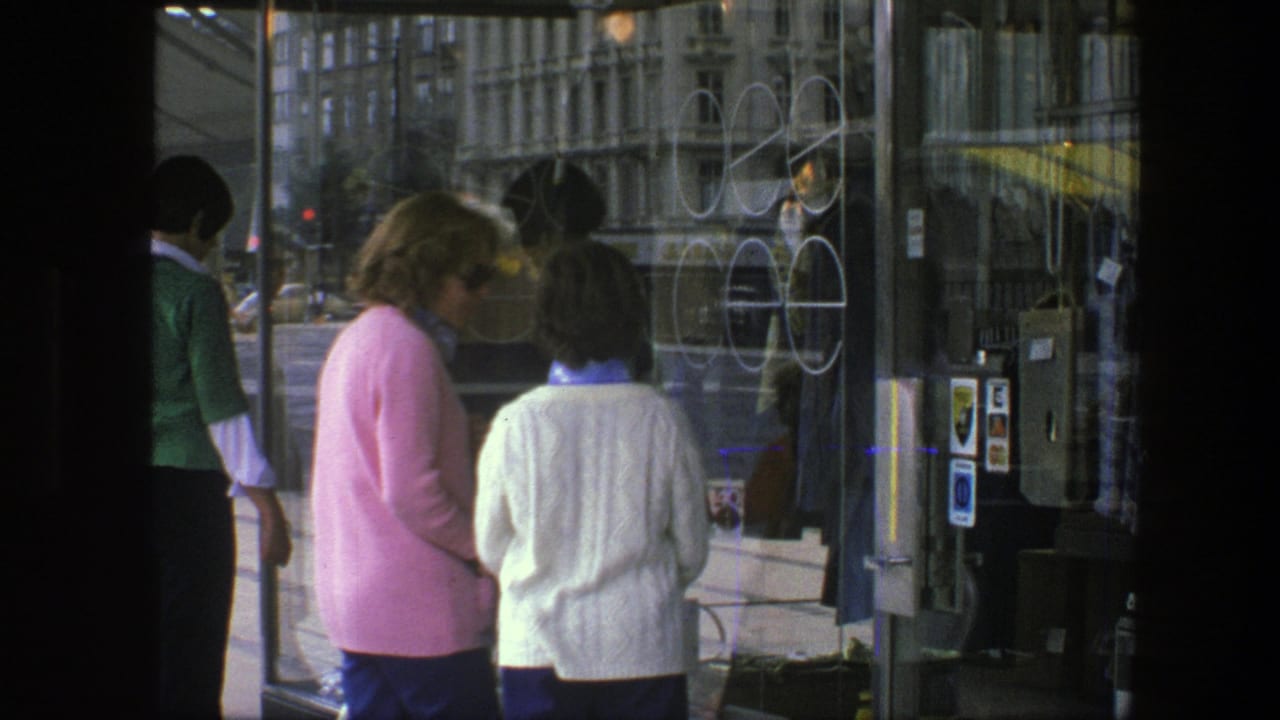 The women continue browsing a Copenhagen shop window in 1975, with glass reflections, display signage, and nearby pedestrians visible.
