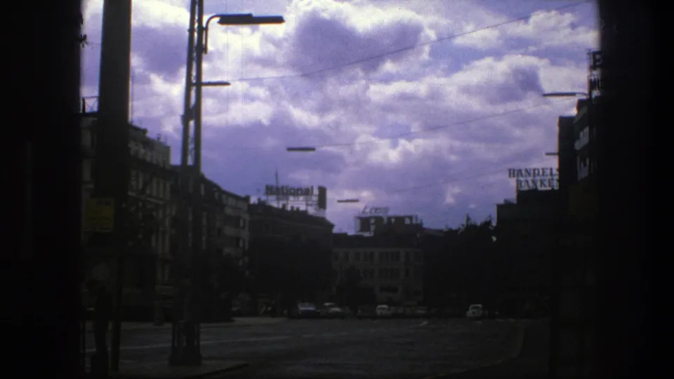 A wide Copenhagen street view from 1975 shows older cars, commercial buildings, streetlamps, signs, and a dramatic cloudy sky.