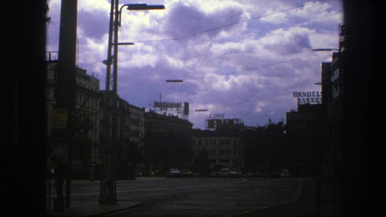 Cloudy Copenhagen street framed by dark vertical edges with rooftop National and Handelsbanken signs.