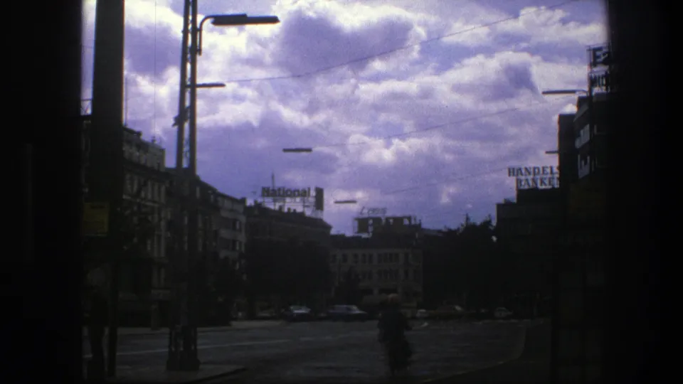 1975 Copenhagen street scene with a cyclist crossing the lower frame, silhouetted edges, overhead lamps, cars, and rooftop National and Handelsbanken signs.