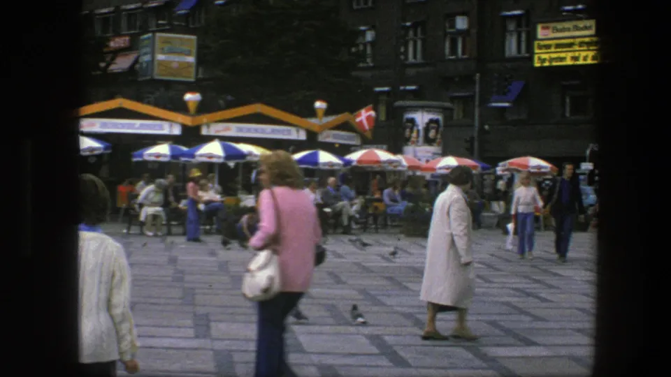 1975 Copenhagen street view showing pedestrians in the square, outdoor cafe seating, visible signs, and a woman in a white coat.
