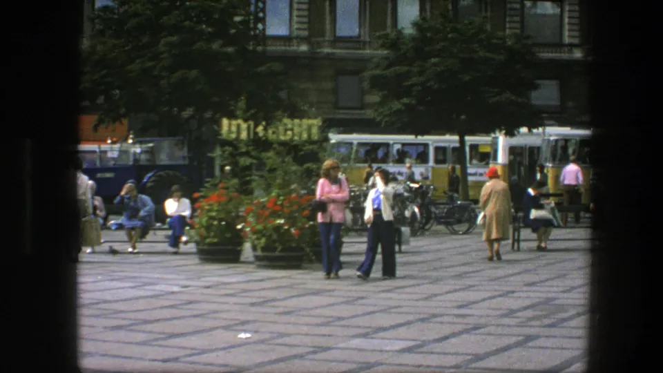 A 1975 Copenhagen plaza view shows pedestrians moving past benches and planters with bicycles and vintage buses in the background.