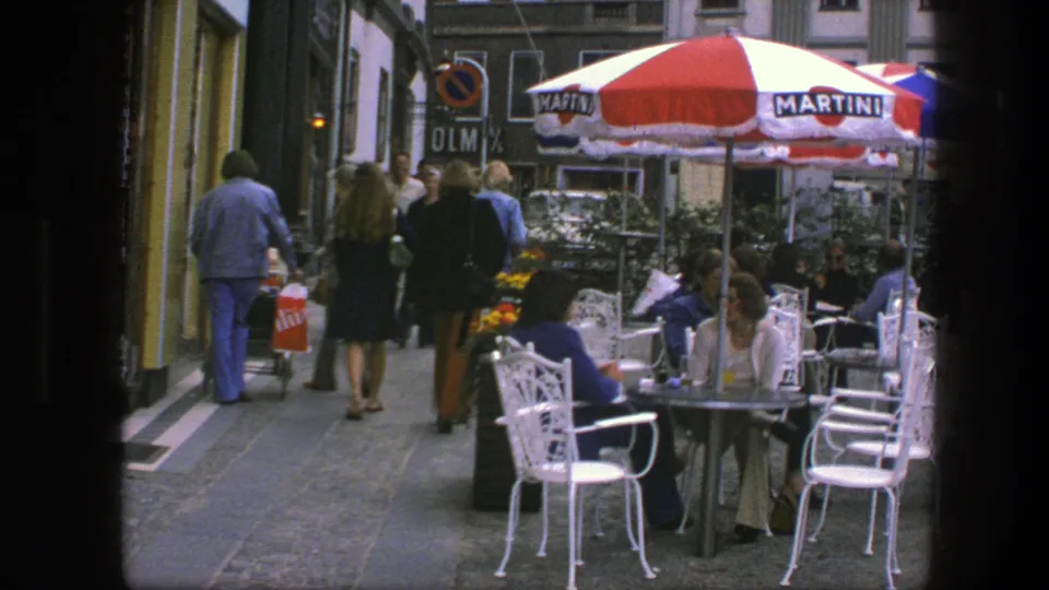 A Copenhagen sidewalk scene from 1975 shows pedestrians beside outdoor cafe tables and a red-and-white Martini-branded umbrella.