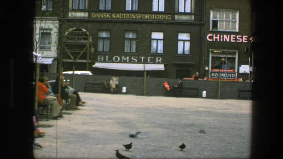 1975 Copenhagen square with pigeons on the pavement, benches, pedestrians, Blomster signage, and a Chinese restaurant facade.