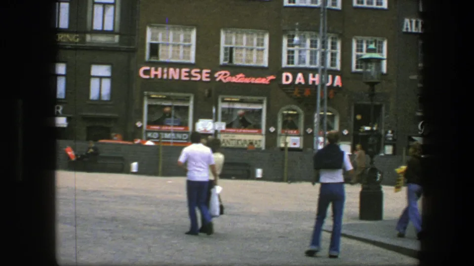 1975 Copenhagen square scene with pedestrians, benches, a lamppost, storefront windows, and bright Chinese restaurant signage across the street.