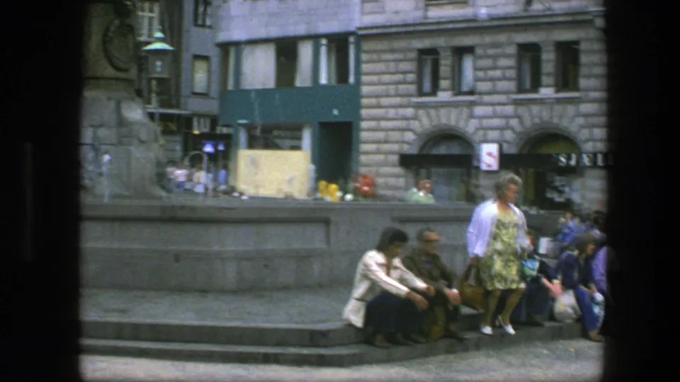 Copenhagen square view with seated pedestrians on stone fountain steps, a woman in patterned clothing, and stone-fronted buildings behind.