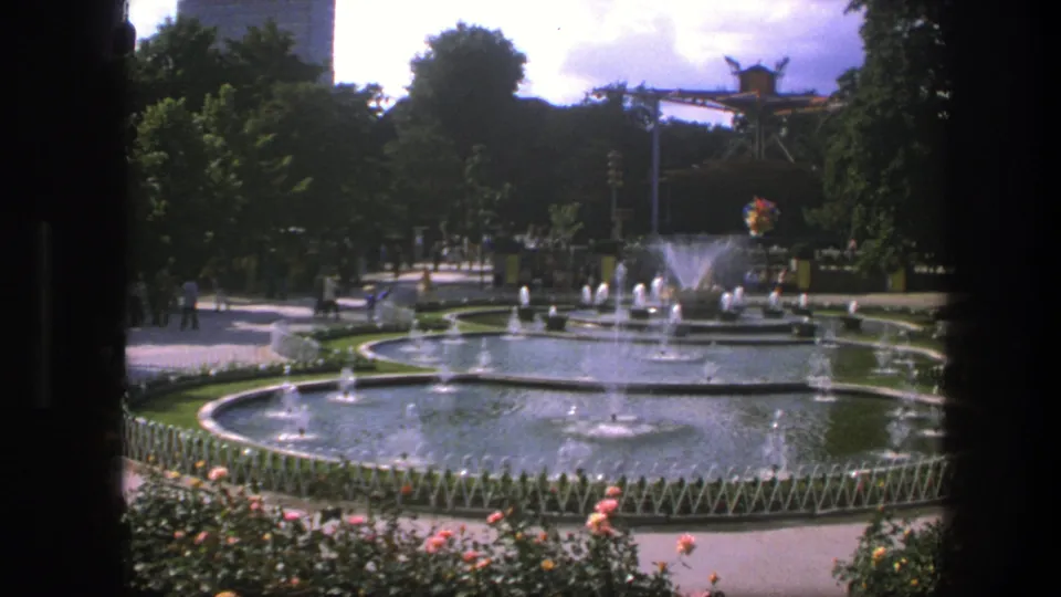 1975 Copenhagen park view with interconnected circular fountains, water jets, flower beds, trees, walkways, and distant visitors.