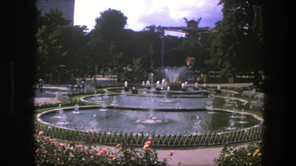 1975 Copenhagen fountain scene with multiple circular basins, spraying jets, garden planting, shaded paths, and distant park visitors.